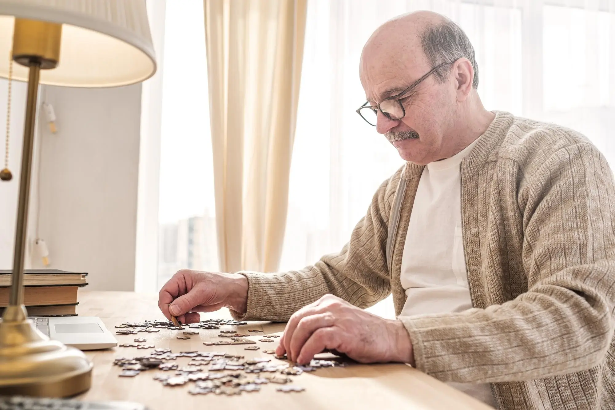 alter Mann mit Brille puzzelt am Schreibtisch